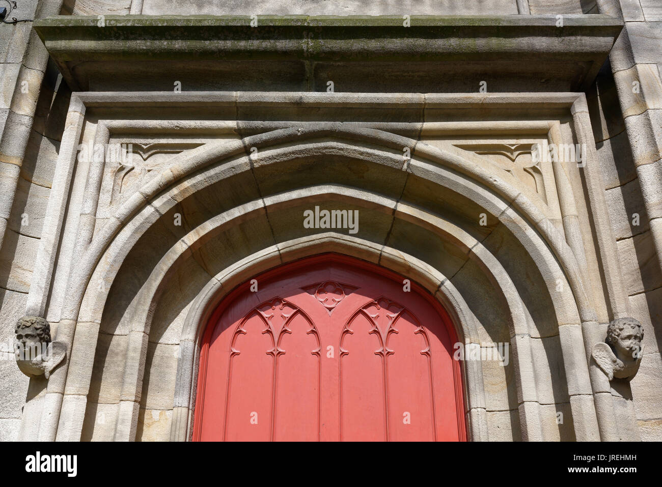 Ornate stone arched doorway with red wooden door, all saints stand church, whitefield, Stock Photo