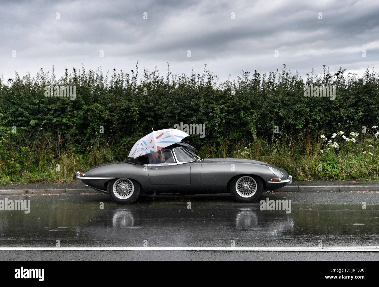 Alfriston, East Sussex. 5th August 2017. Jaguar E-Type driver caught out by a sudden heavy downpour in East Sussex on a day of mixed weather. © Peter Cripps/Alamy Live News Stock Photo