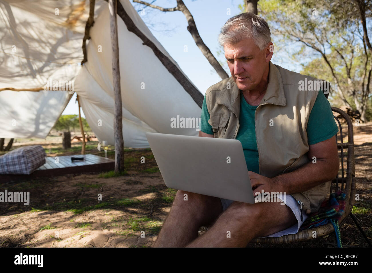 Mature man using laptop while sitting on chair at campsite Stock Photo