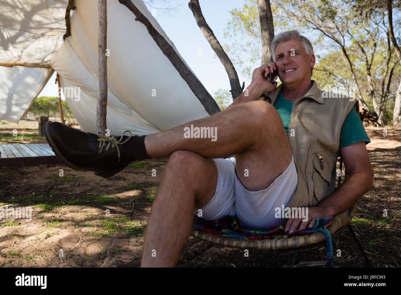 Mature man talking on phone while sitting on chair at campsite Stock Photo