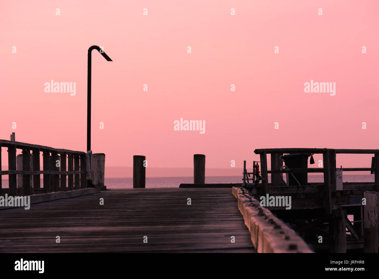 Pink sunset hues over wooden jetty wharf on Fraser Island Queensland Australia Stock Photo