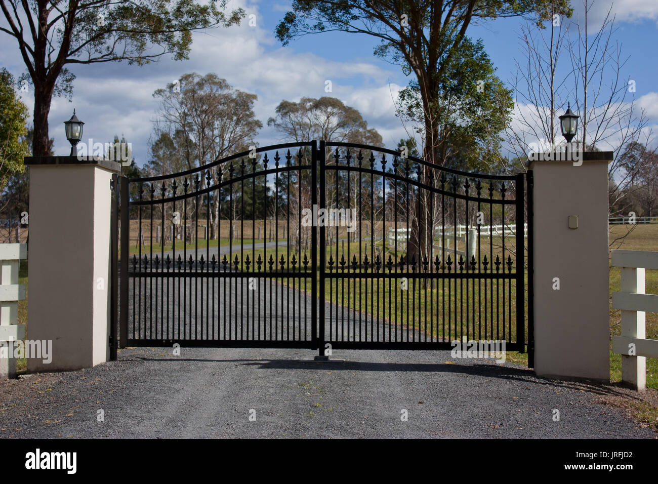 Black metal driveway entrance gates set in brick fence with garden