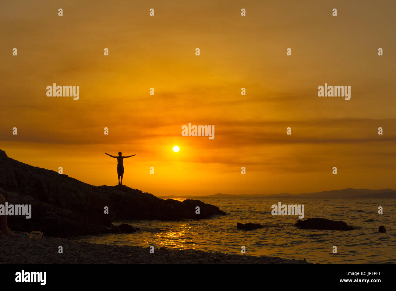 Silhouette of a man with arms raised, at sunset with sun behind him ...