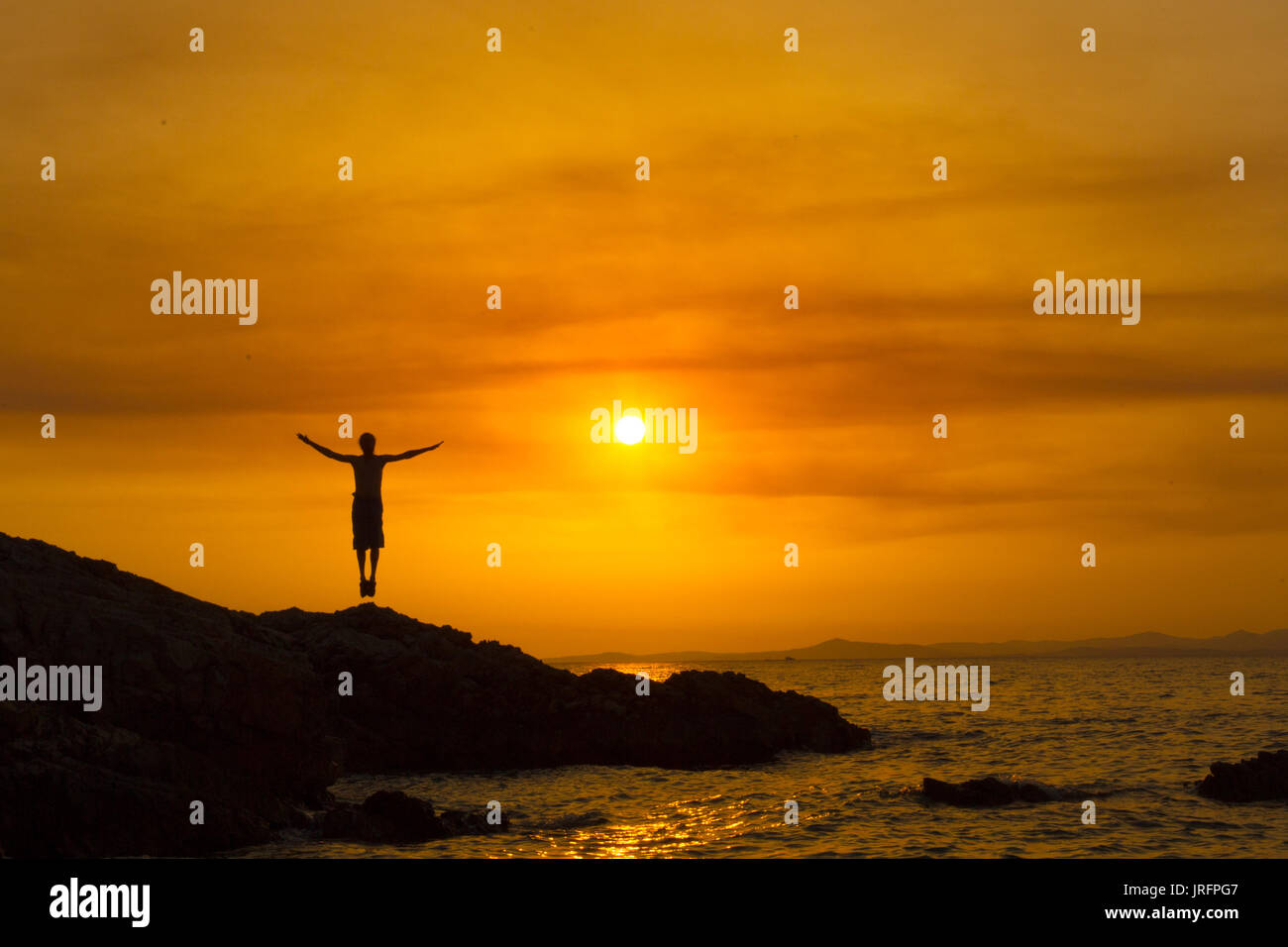 Silhouette of a man with arms raised, at sunset with sun behind him ...