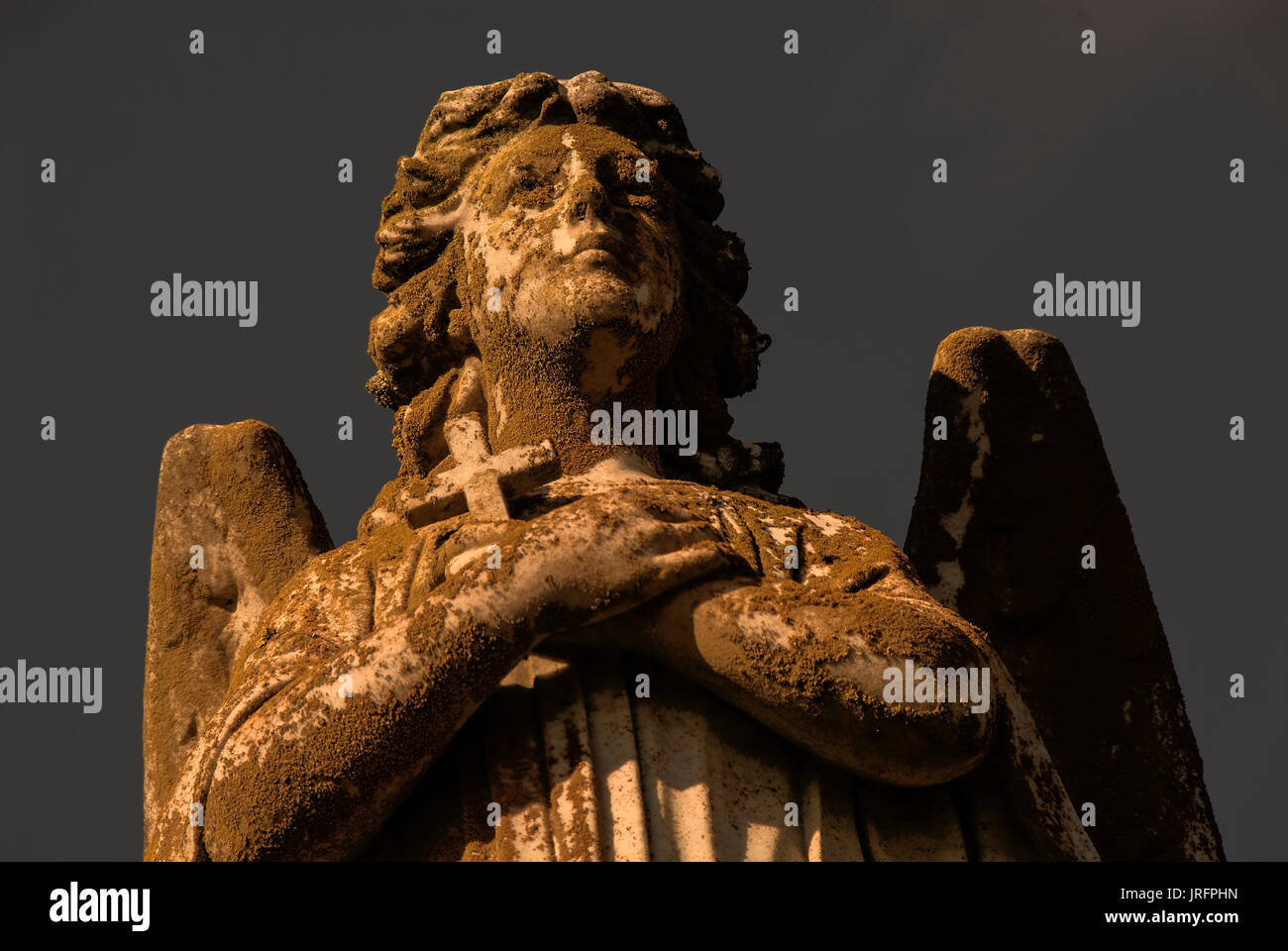 A statue of a male angel with wings holding a small cross. Stock Photo