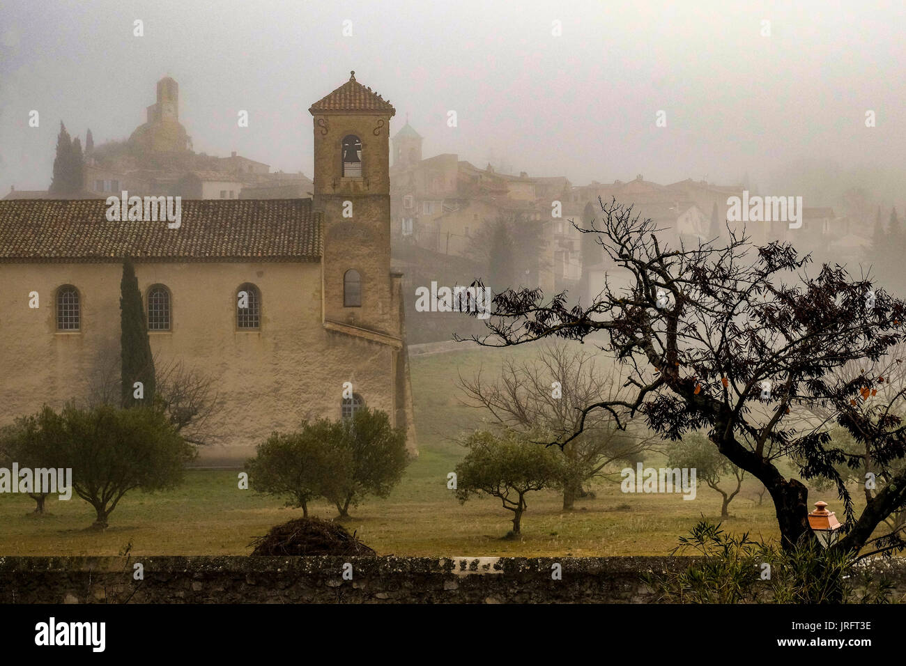 A foggy winter's day in the churchyard of the Provencal town of Lourmarin in the Luberon region of southern France with the village in the background. Stock Photo