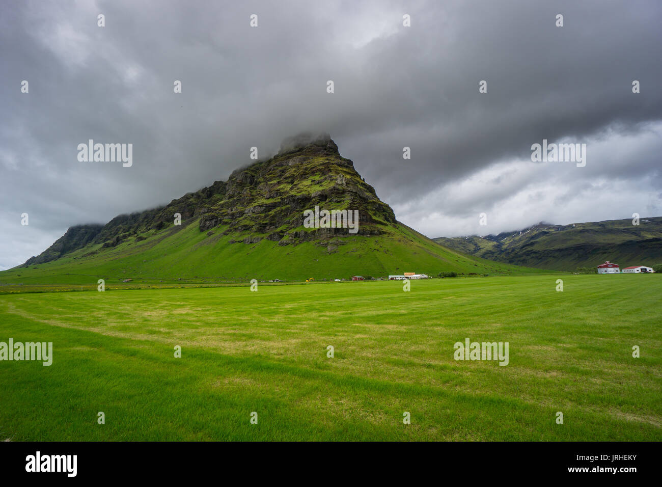 Iceland - Moss covered mountain behind green field with houses Stock ...