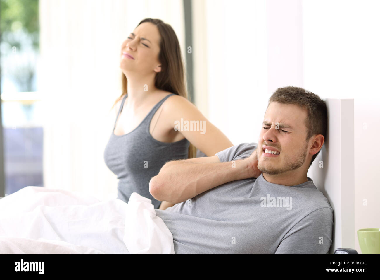 Couple waking up suffering ache after a bad night in a not comfortable bed at home or hotel room Stock Photo