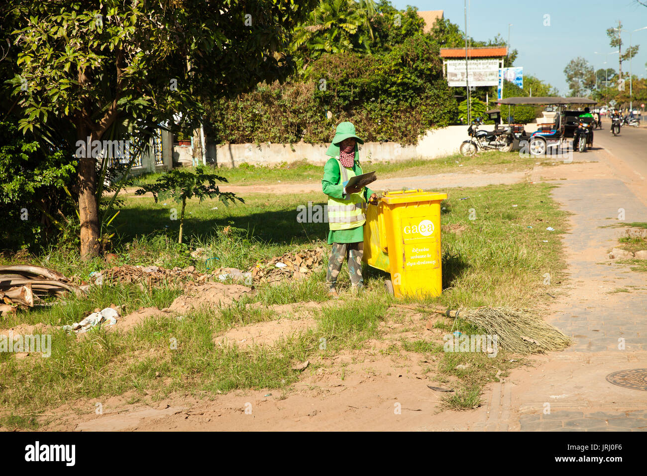 Woman worker garbage collector shakes out trash on the pedestrian sidewalk lawn after cleaning the road in the city siem reap / Cambodia Stock Photo