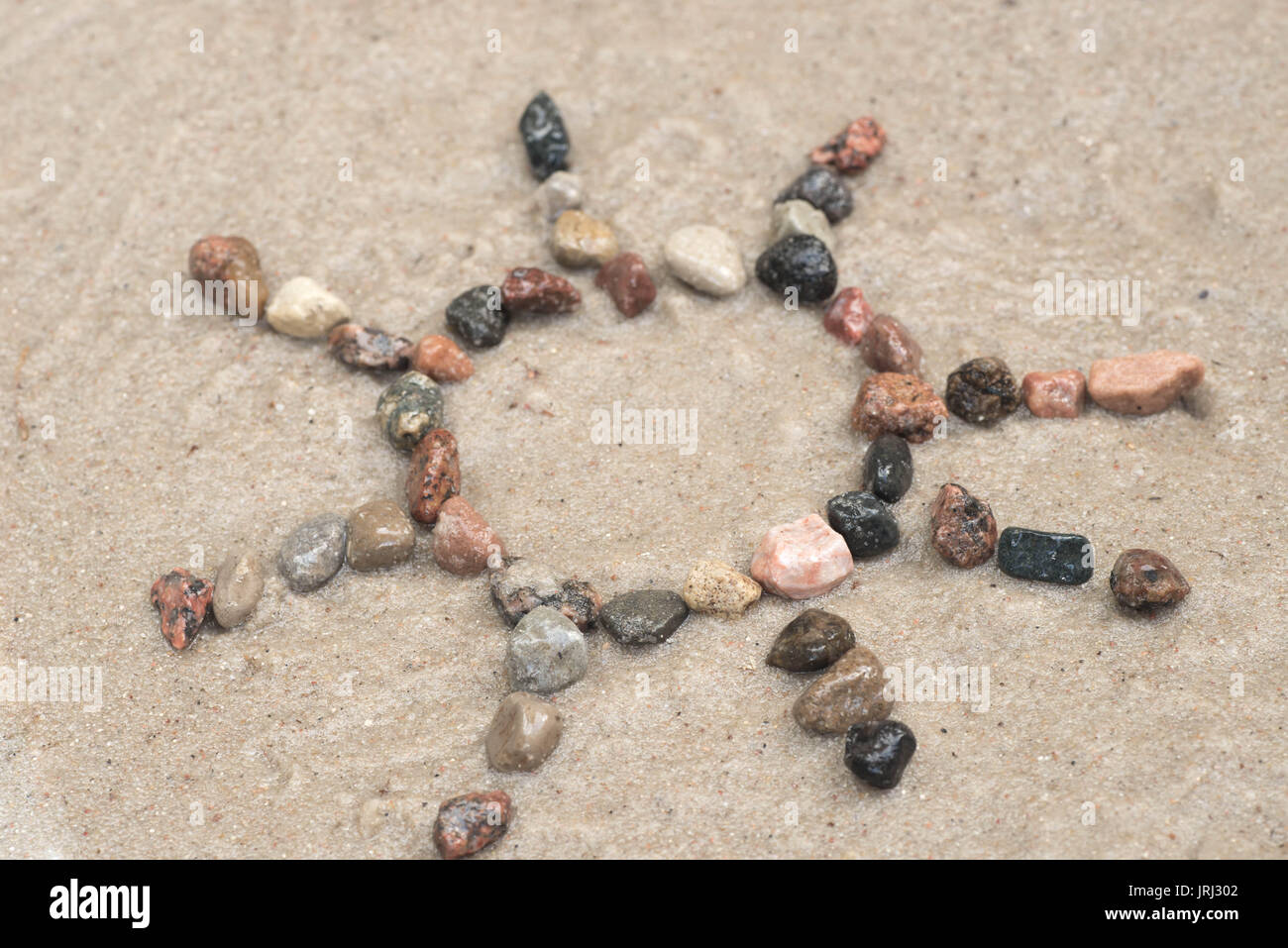 pebble sun sign on sand background Stock Photo