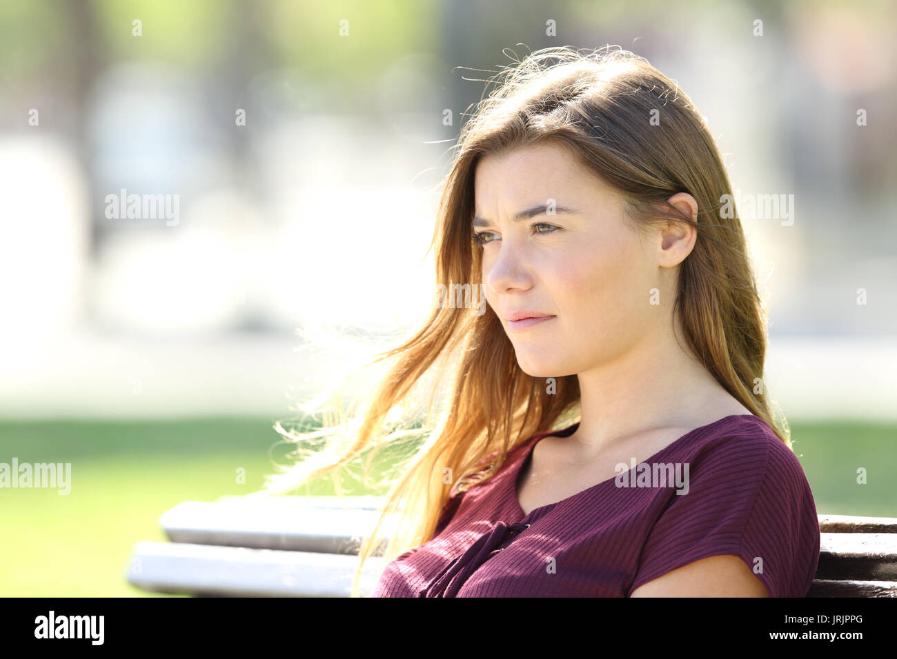 Portrait of a serious girl sitting on a bench thinking and looking away outdoors Stock Photo