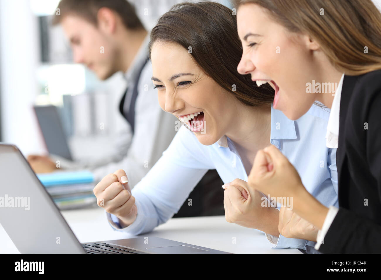 Excited executives reading on line news in a laptop at office Stock Photo