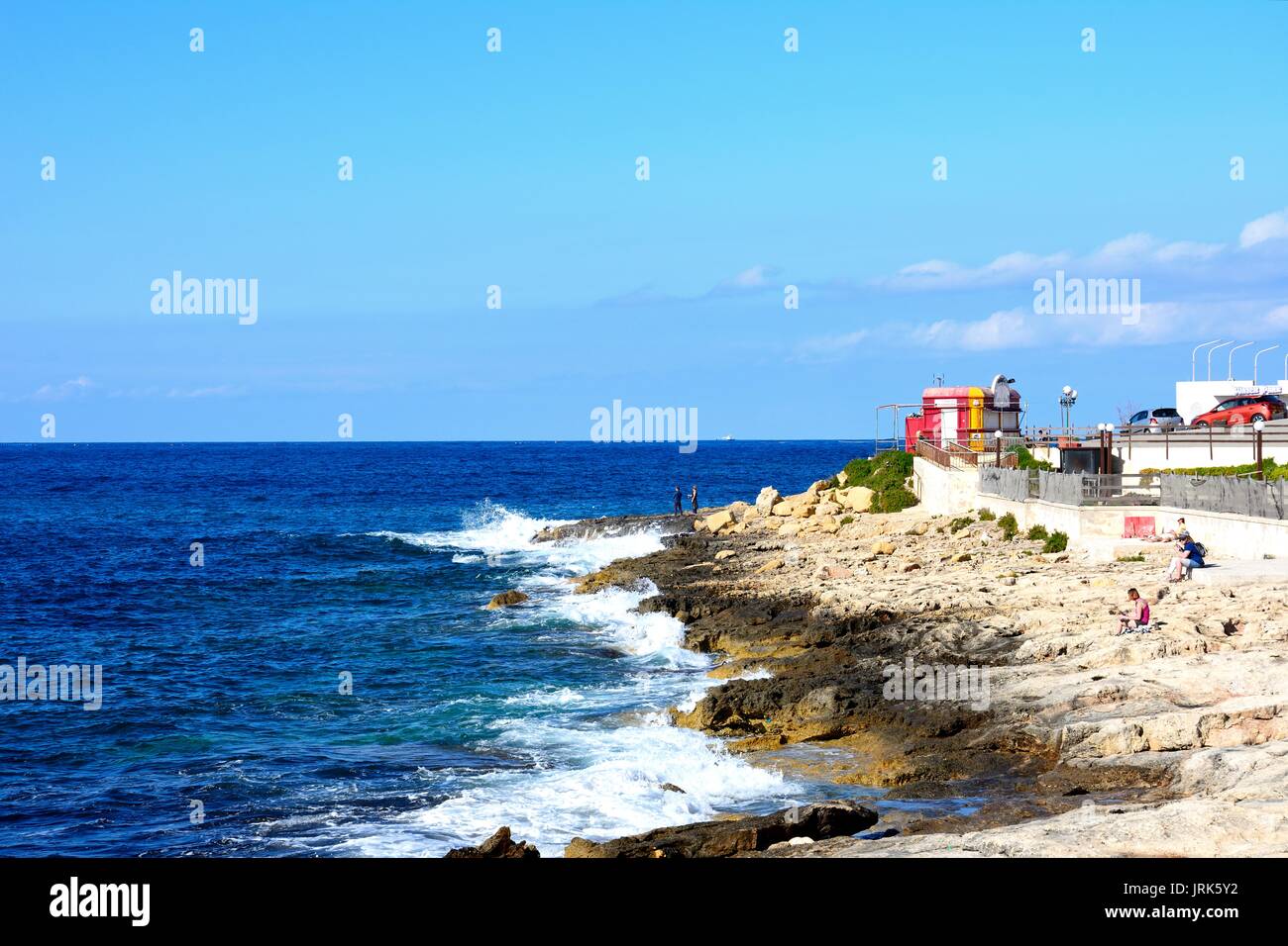Tourists relaxing on the rocky shoreline, Bugibba, Malta, Europe. Stock Photo