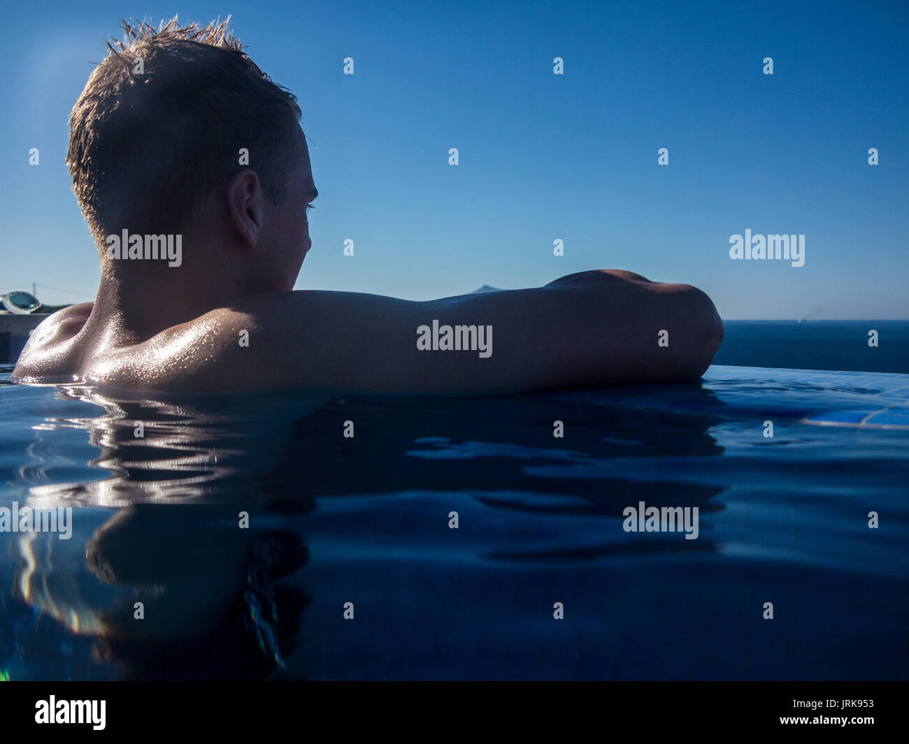 A muscular teenager enjoys the view in an infinity pool Stock Photo