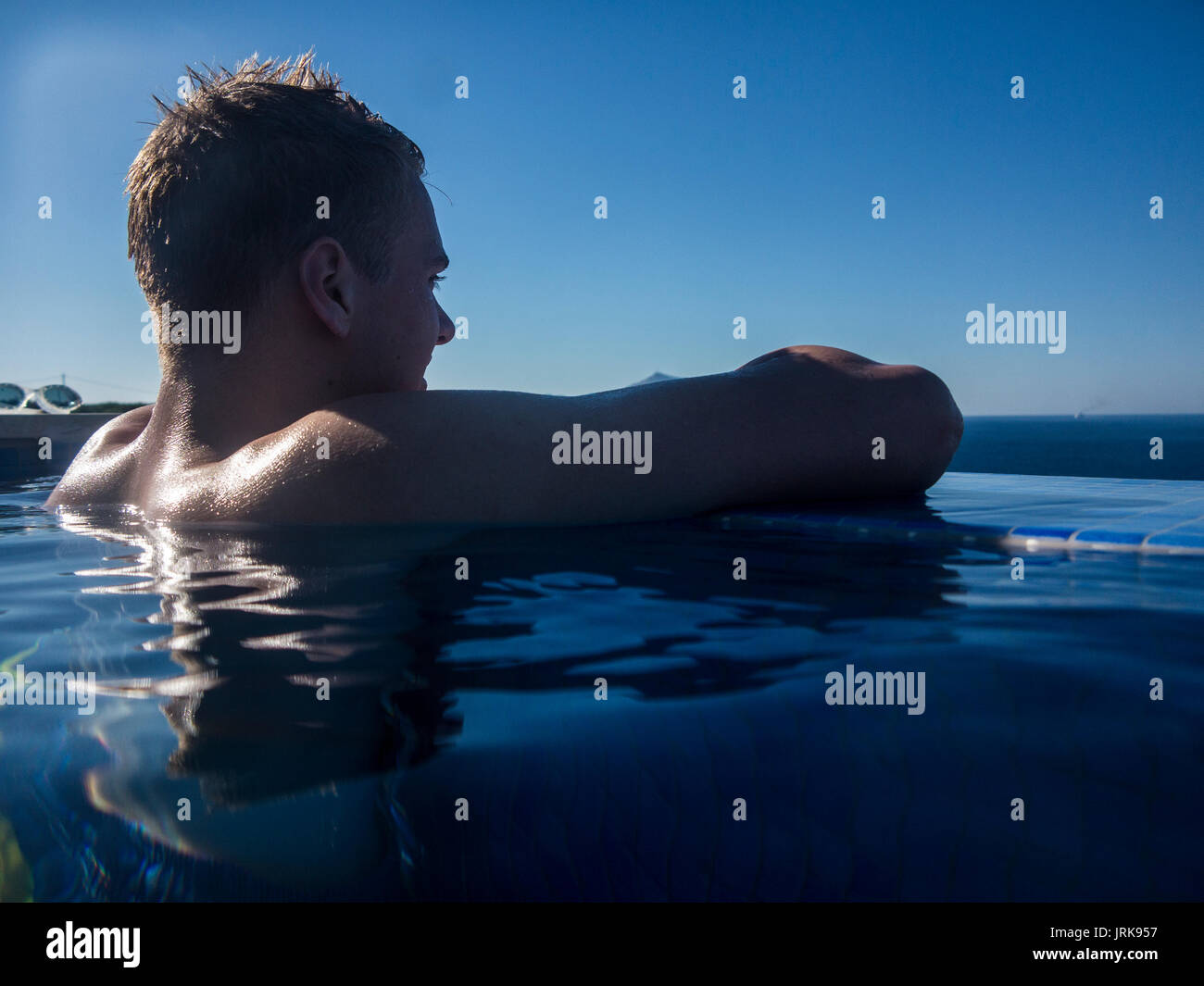 A muscular teenager enjoys the view in an infinity pool Stock Photo