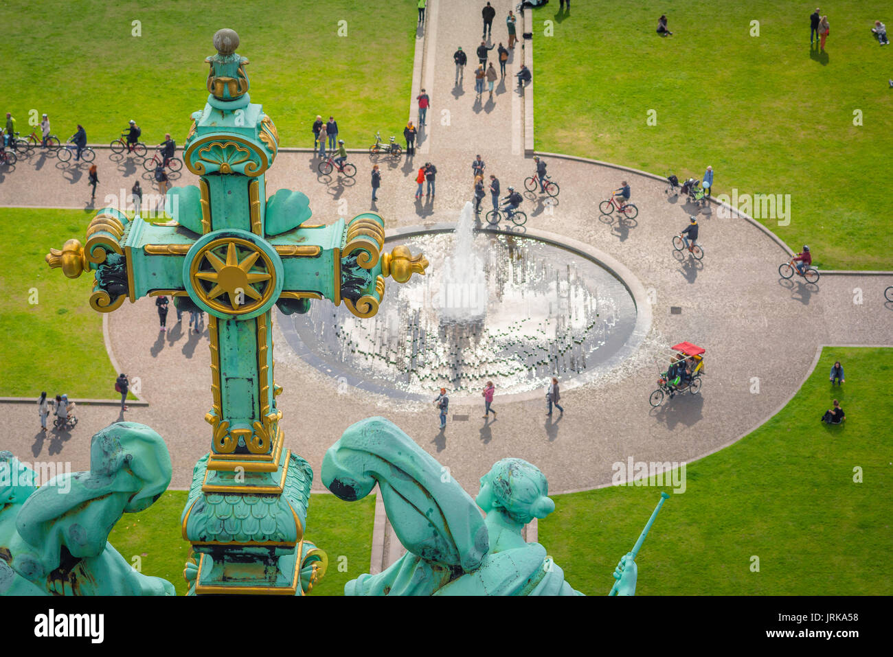 Berlin park, view past the Berliner Dom Cathedral's ornate crucifix towards people cycling or walking through the Lustgarten park, Berlin, Germany. Stock Photo