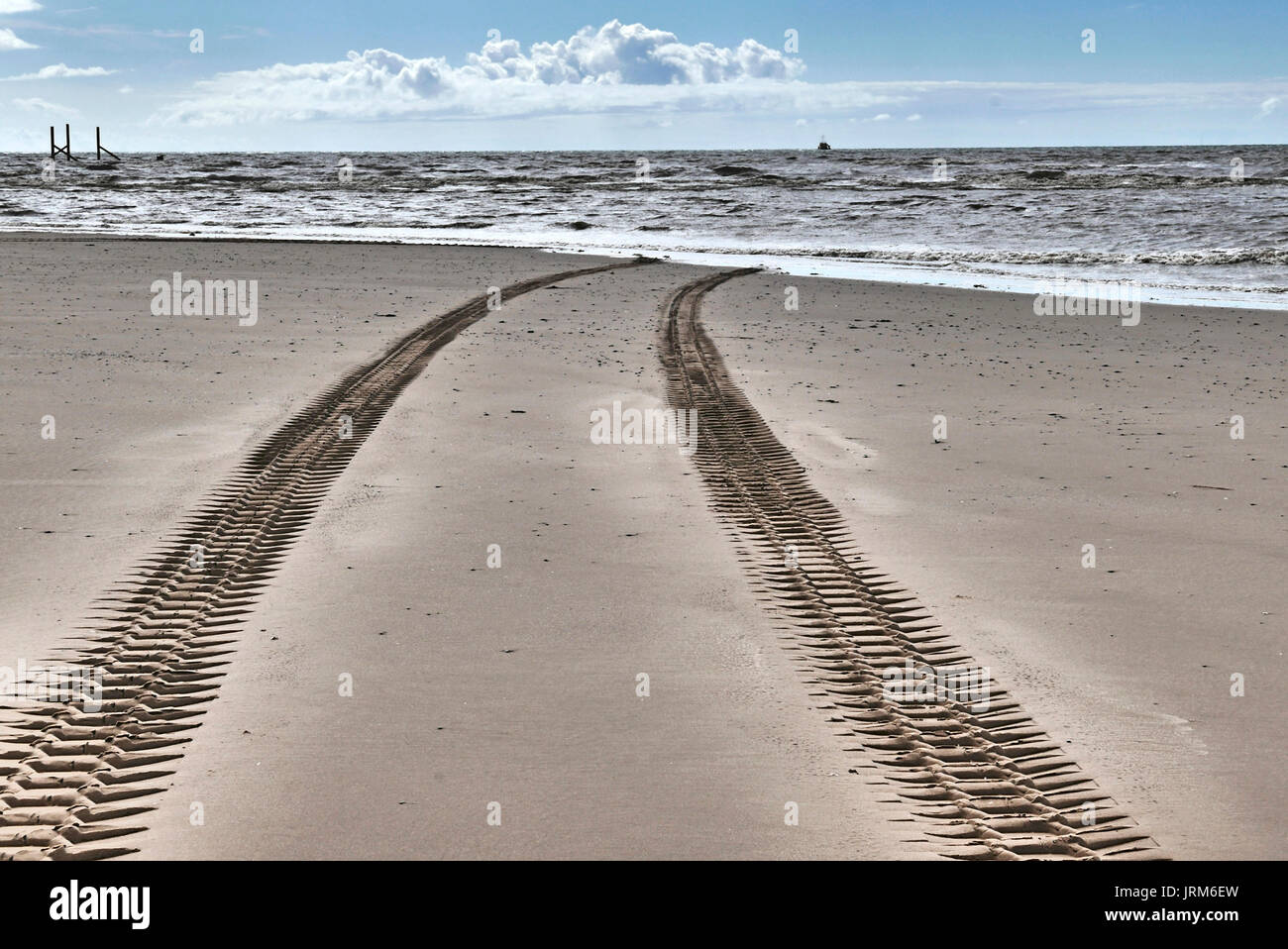 Large vehicle tyre tracks on beach disappearing into the sea Stock Photo