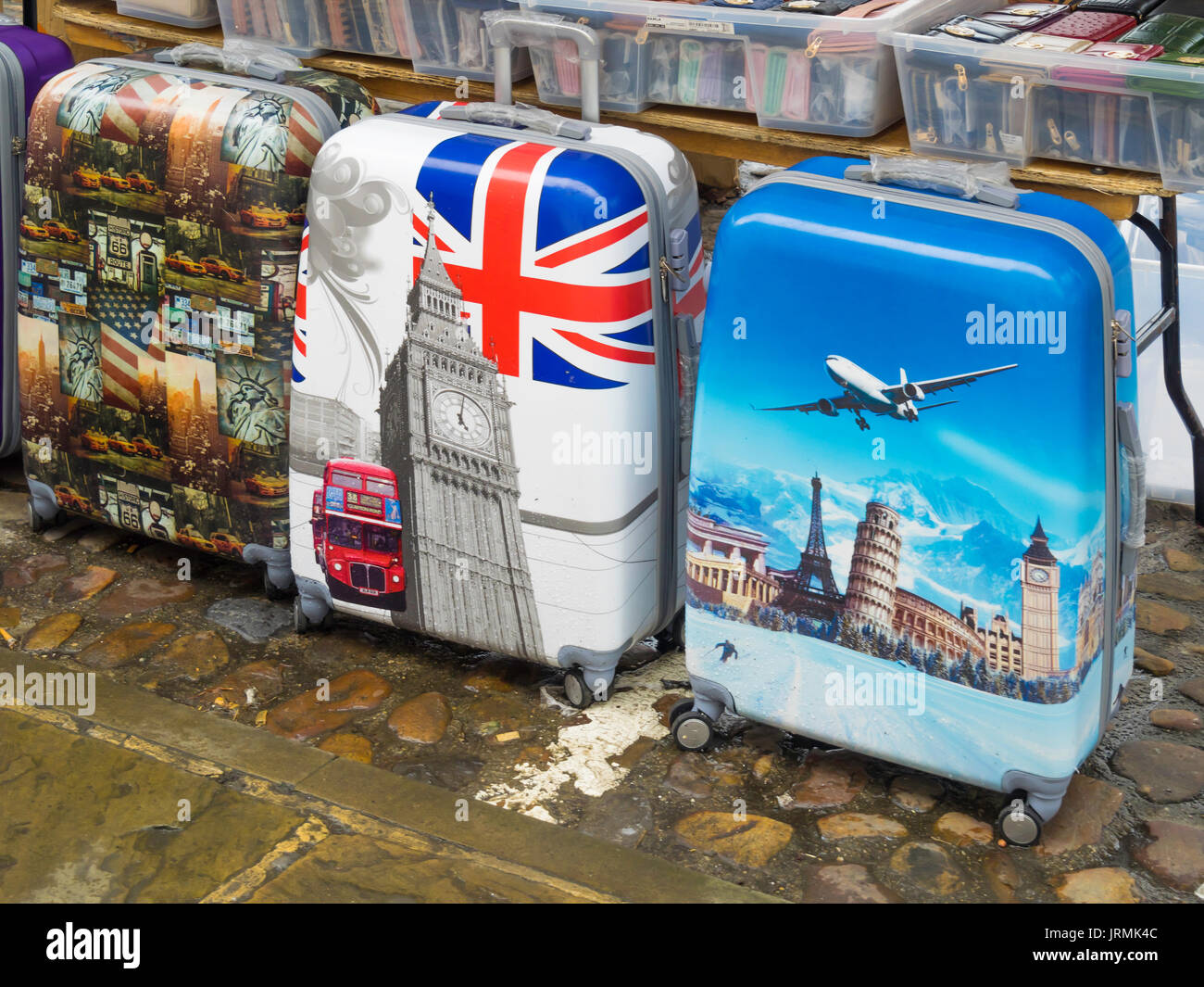 Cheap Holiday Pull along suitcases decorated with British American and International scenes for sale in an English Street Market Stock Photo