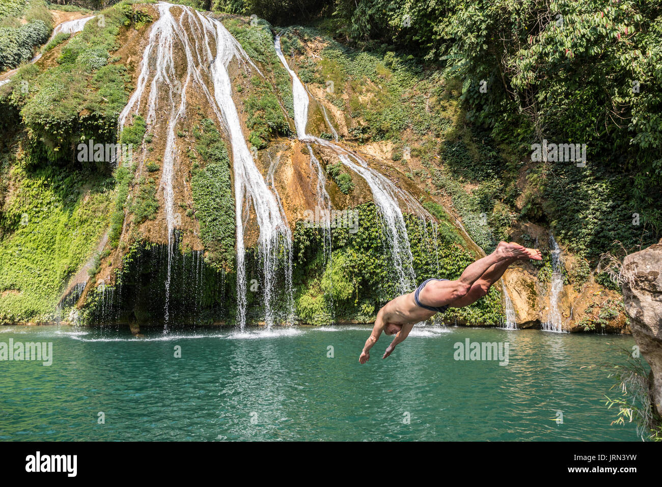 Man diving into a pool at the base of a waterfall in a remote area of Meghalaya, India Stock Photo