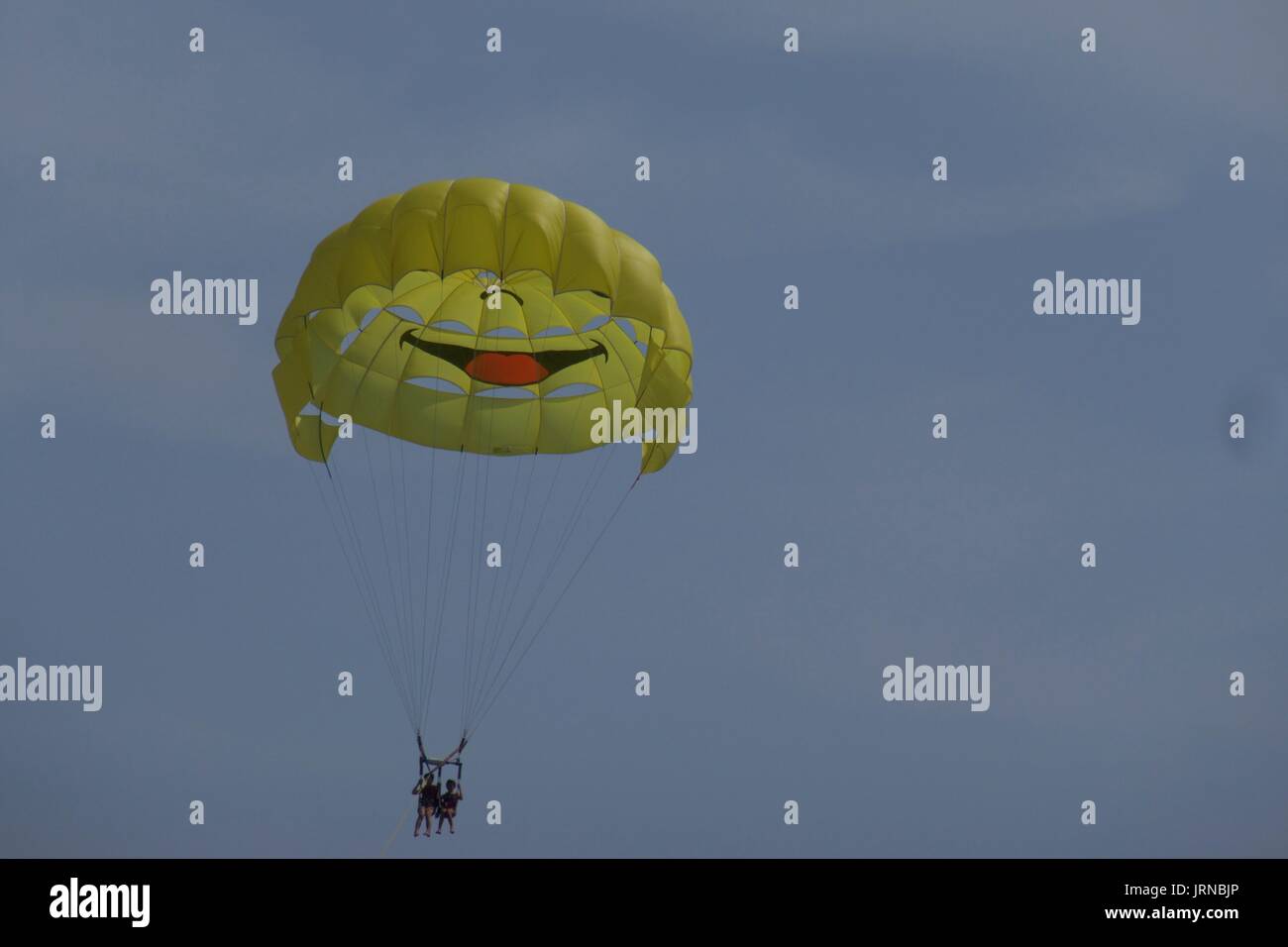Parasailing with yellow smiley face parasail against cloudy sky, Nice, France Stock Photo