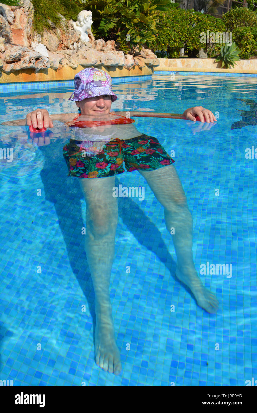 Keeping cool! Woman floating in a swimming pool, using a pool noodl. Stock Photo