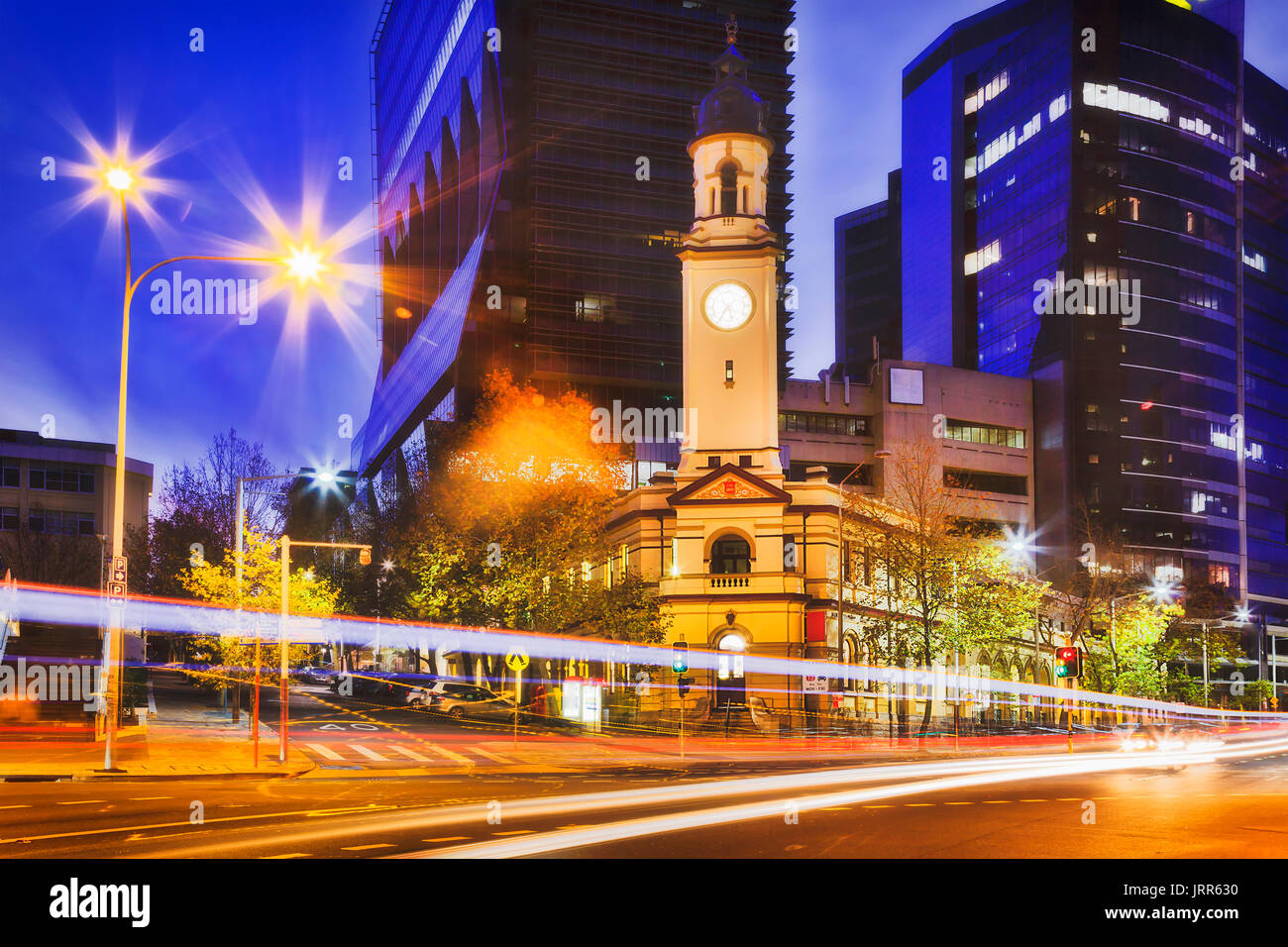 Historic heritage North Sydney post office building with clock tower against tall modern business high-rises at sunset on car traffic street. Stock Photo