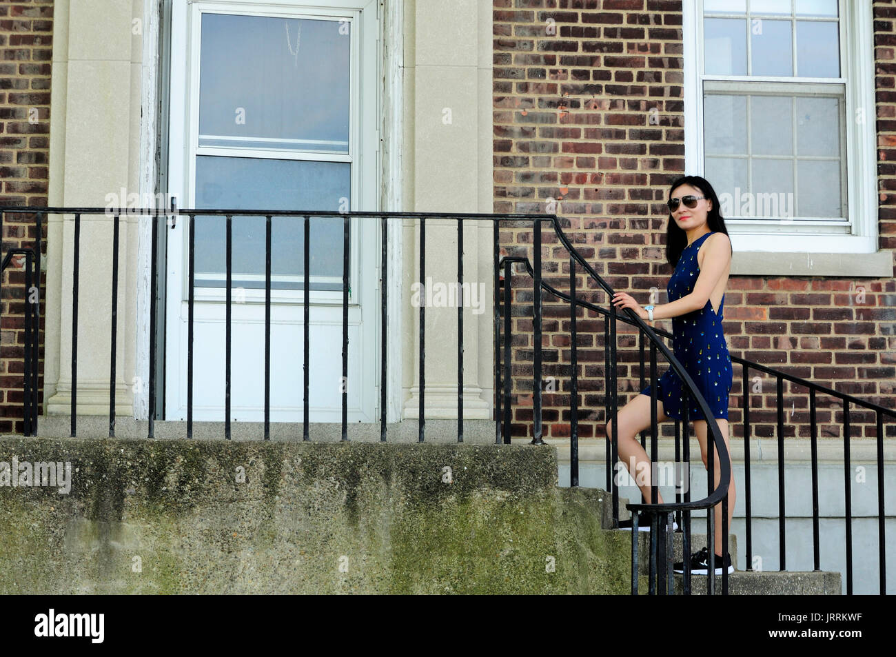 A chinese woman walking up cement steps to the door within a brick building on governors island in New York City, New York. Stock Photo