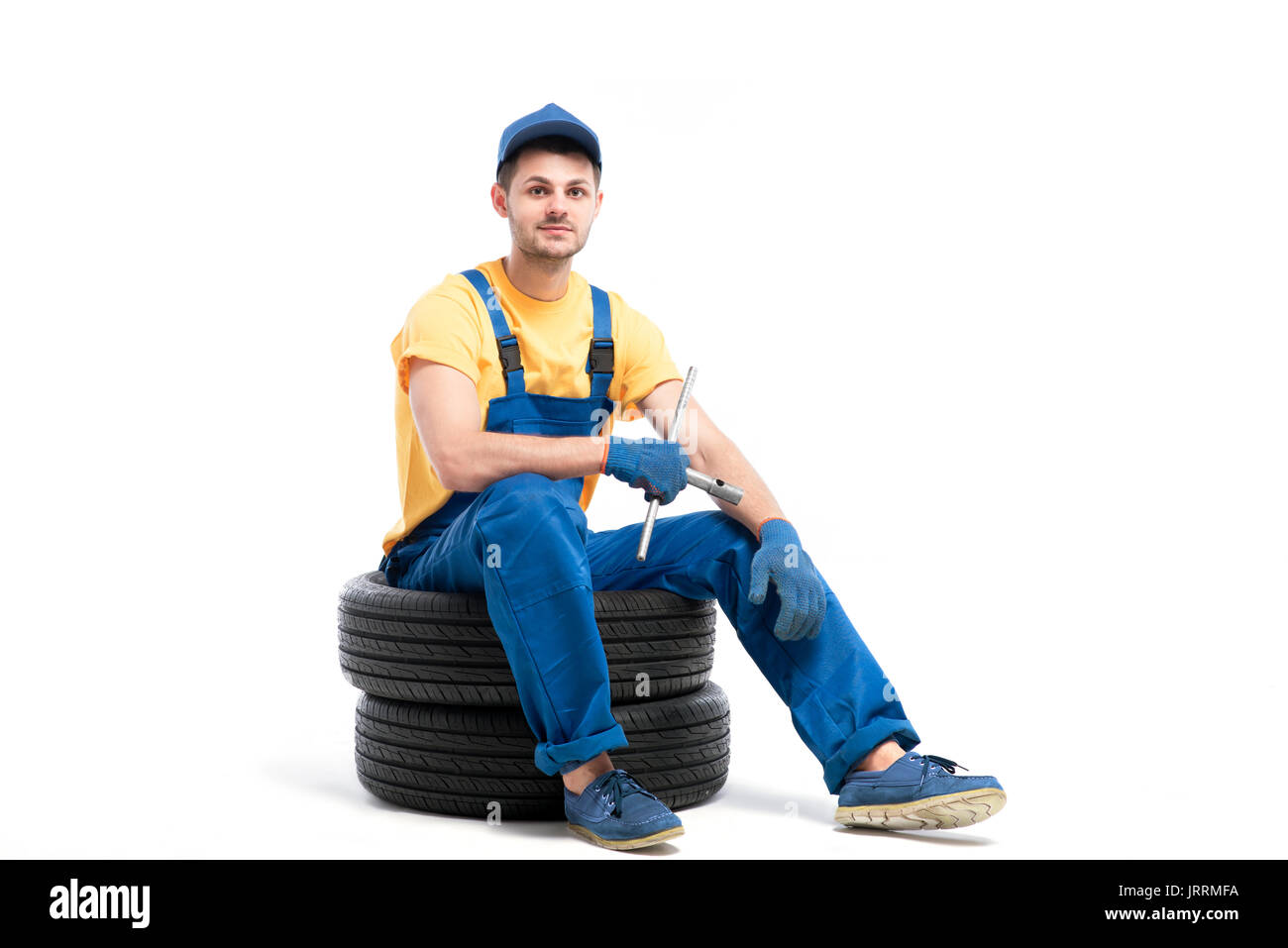 Car tire service, worker in blue uniform sitting on car tyres, white