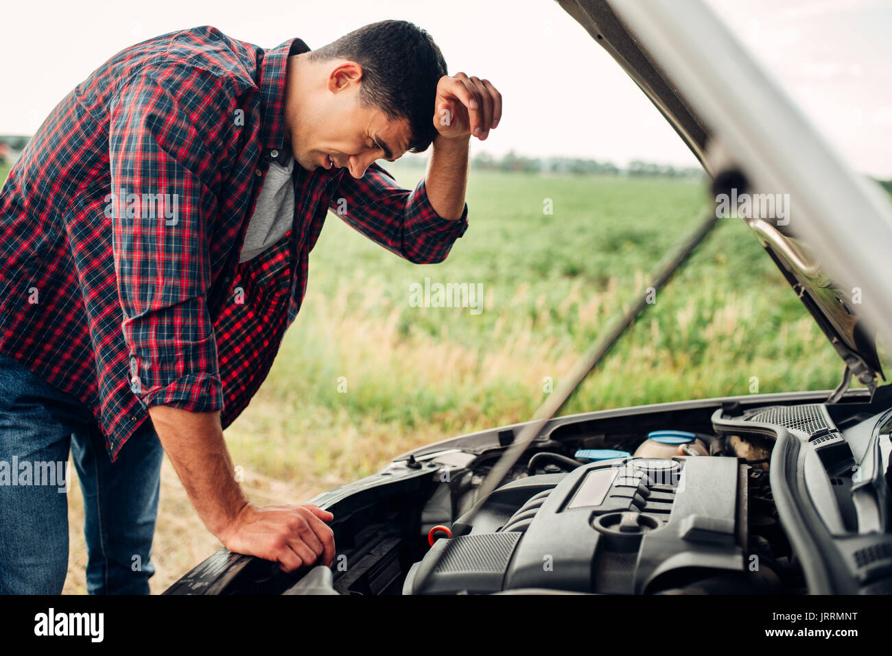 Tired man tries to repair a broken car. Vehicle with open hood on roadside Stock Photo