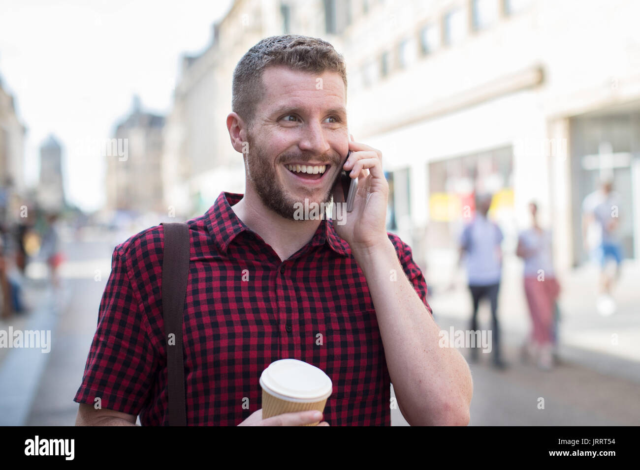 Man Walking Along City Street Talking On Mobile Phone Stock Photo