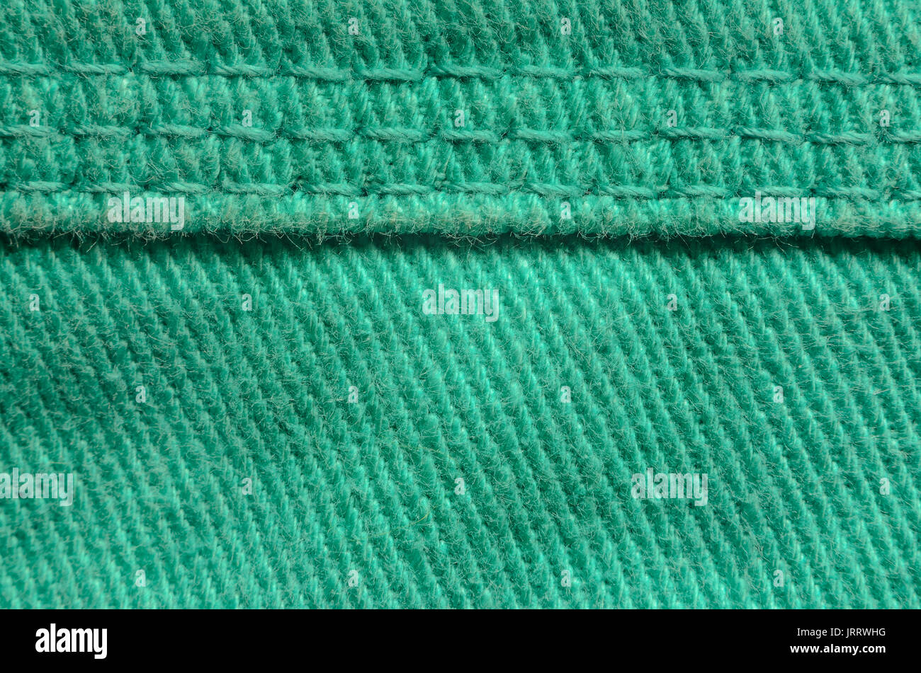 Green Denim Tissue Structure Textile Texture Close-up. Macro shot of the finishing seam on a green jeans product. Stock Photo