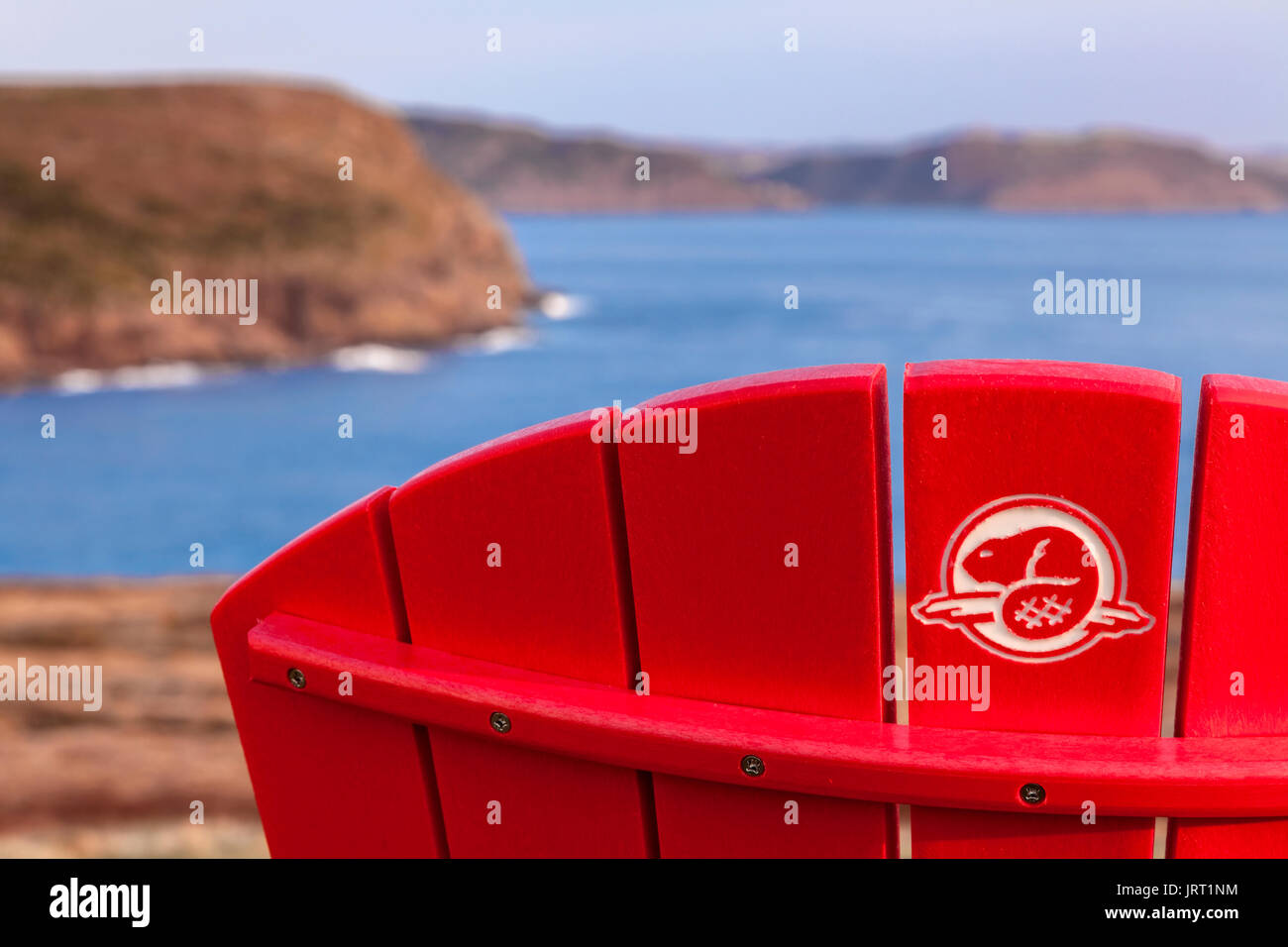 A Parks Canada logo on the back of a red Muskoka chair at Cape Spear National Historic Site of Canada at sunrise. Cape Spear, St. John's, Newfoundland Stock Photo