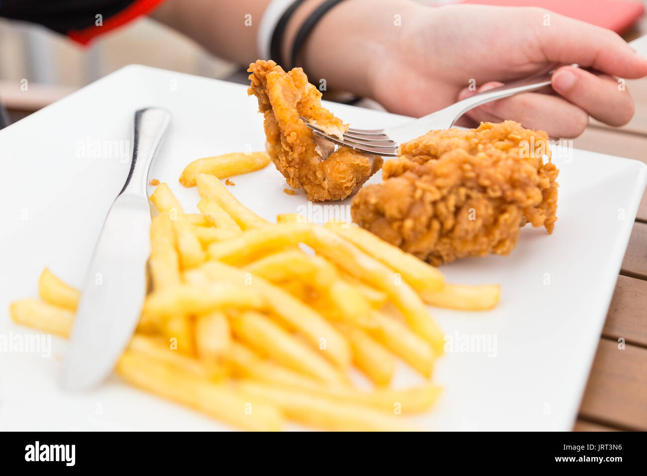 hand holding fork with strip of fried chicken and french fries on a white plate, unhealthy diet, concept picture for food that can hurt your health Stock Photo