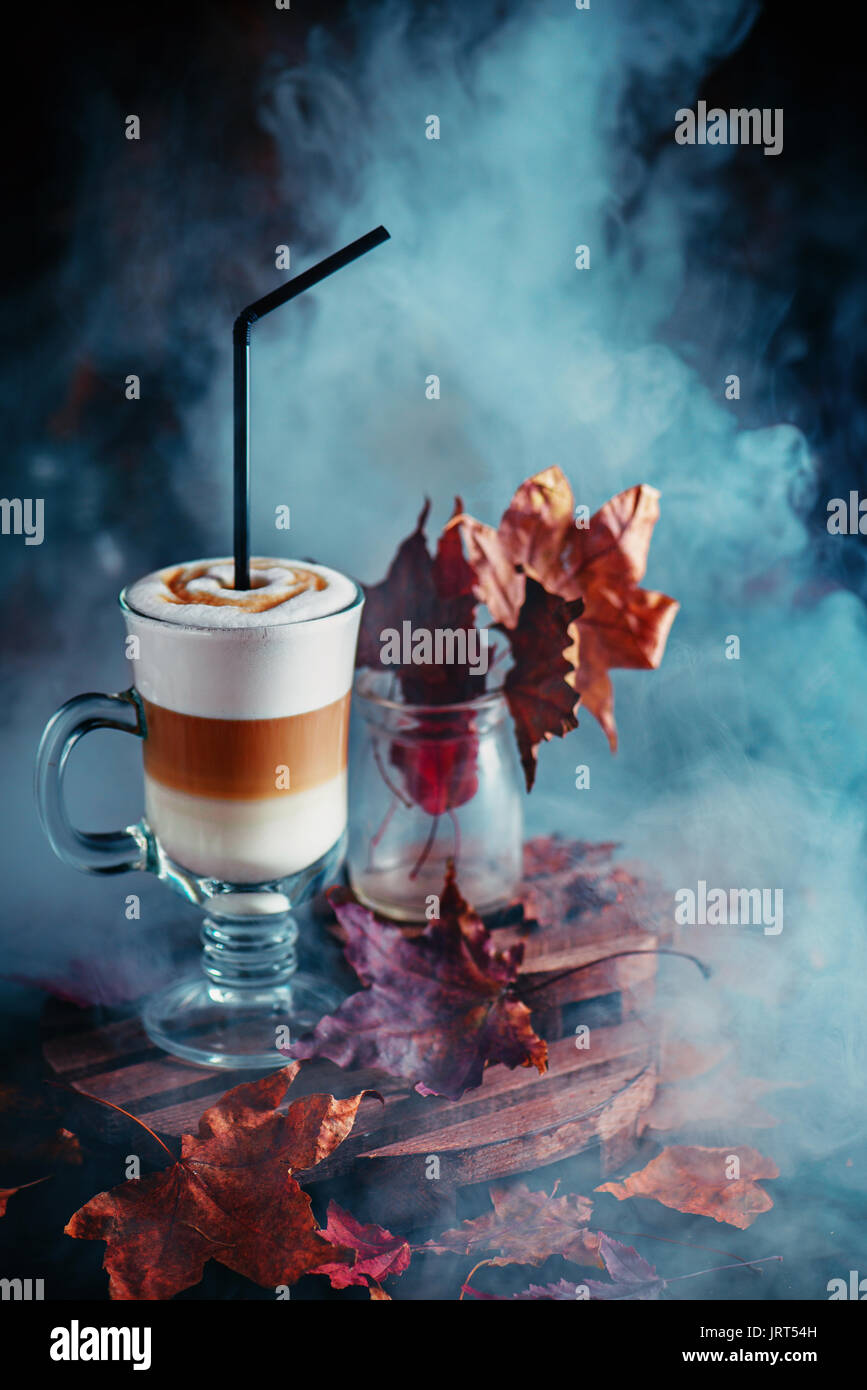 Pumpkin spice layered latte with steam and autumn leaves on a dark wooden background Stock Photo