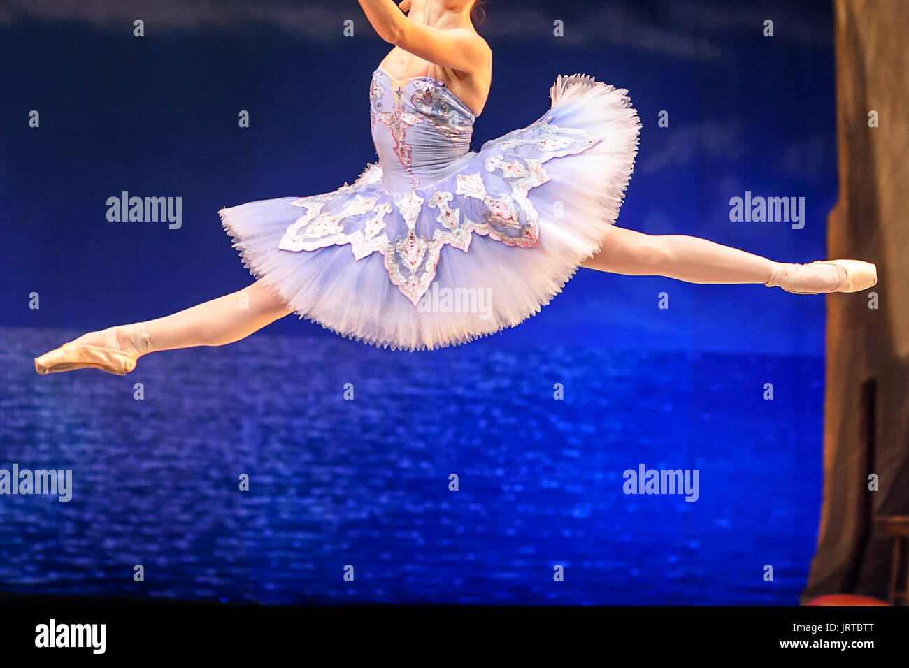 culture, ballet, clothes concept. ballerina, wearing magnificent blue costume with tutu, is in the air, in midflight, doing grand jete, high leap with stretched toes Stock Photo