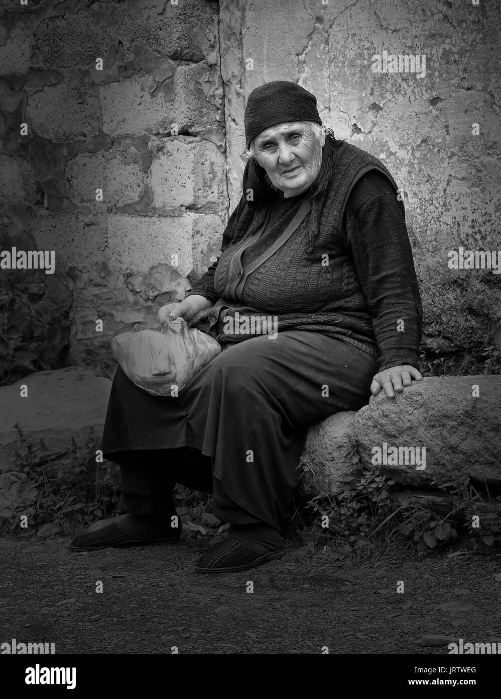 SNO, GEORGIA - JULY 1, 2014: Old woman sitting on a stone in a Caucasian village on July 1, 2014 in Georgia, Europe Stock Photo