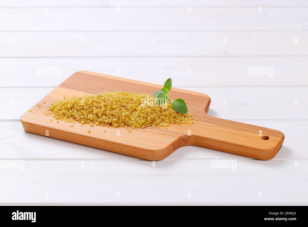 pile of dry wheat bulgur on wooden cutting board Stock Photo