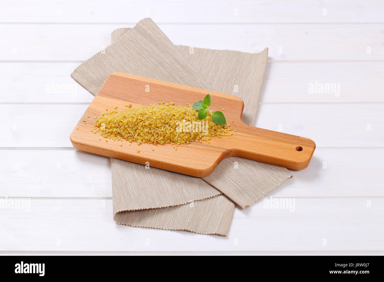 pile of dry wheat bulgur on wooden cutting board Stock Photo
