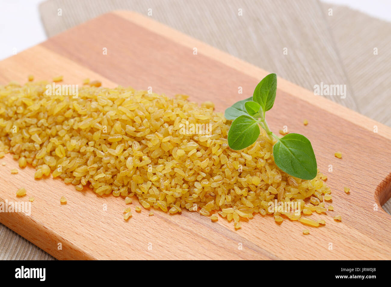 pile of dry wheat bulgur on wooden cutting board - close up Stock Photo