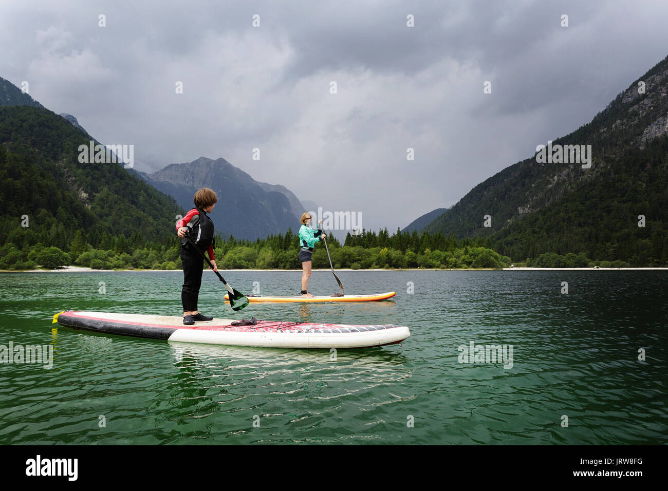Mother and son in a wet suit paddling on SUP on alpine lake, Lago di Predil, Itlay. Stock Photo