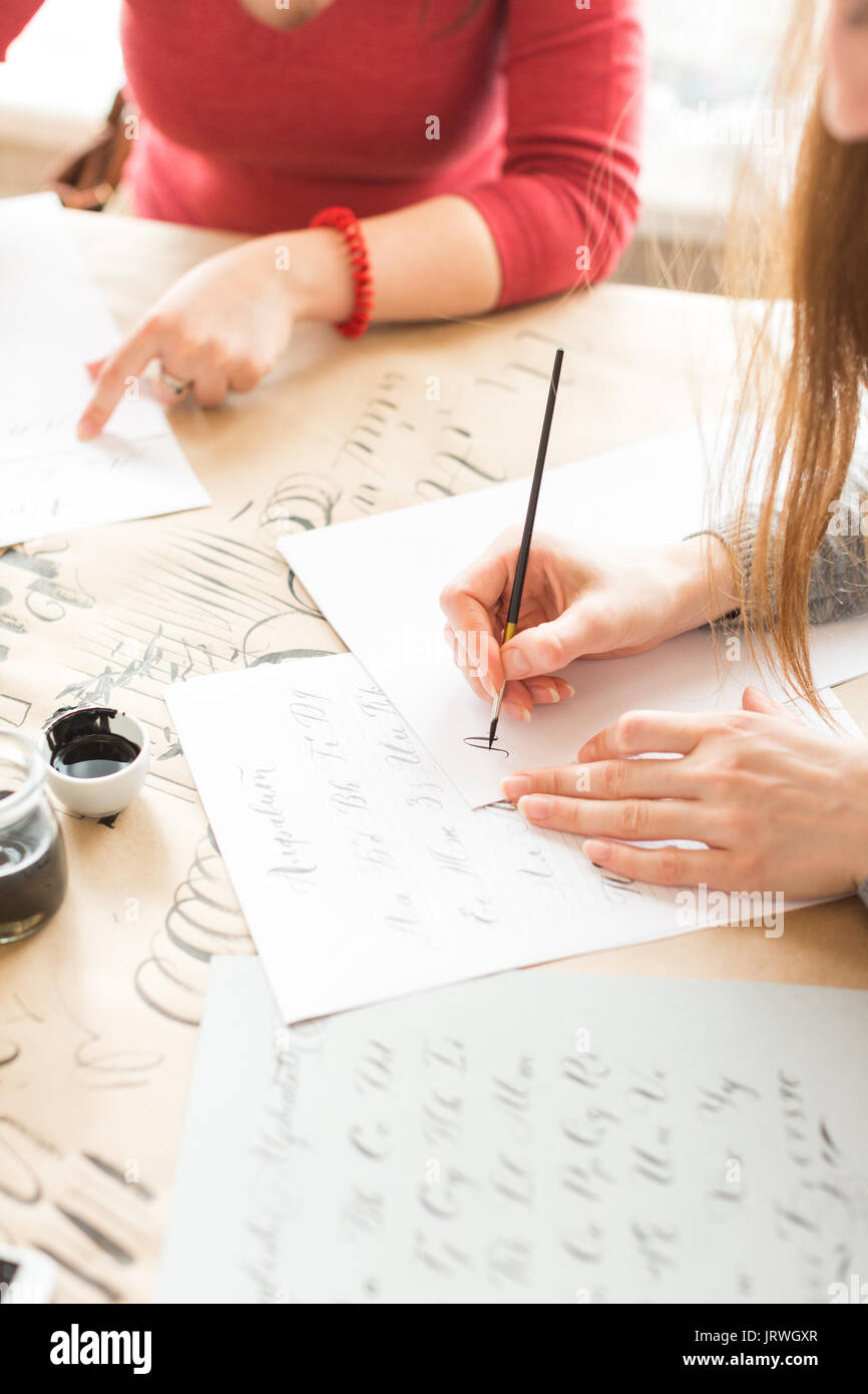 inspiration, patience, lettering concept. two women wearing grey and red sweatshirts creating various fonts with help of special equipment on the desk covered brown paper for sketching Stock Photo