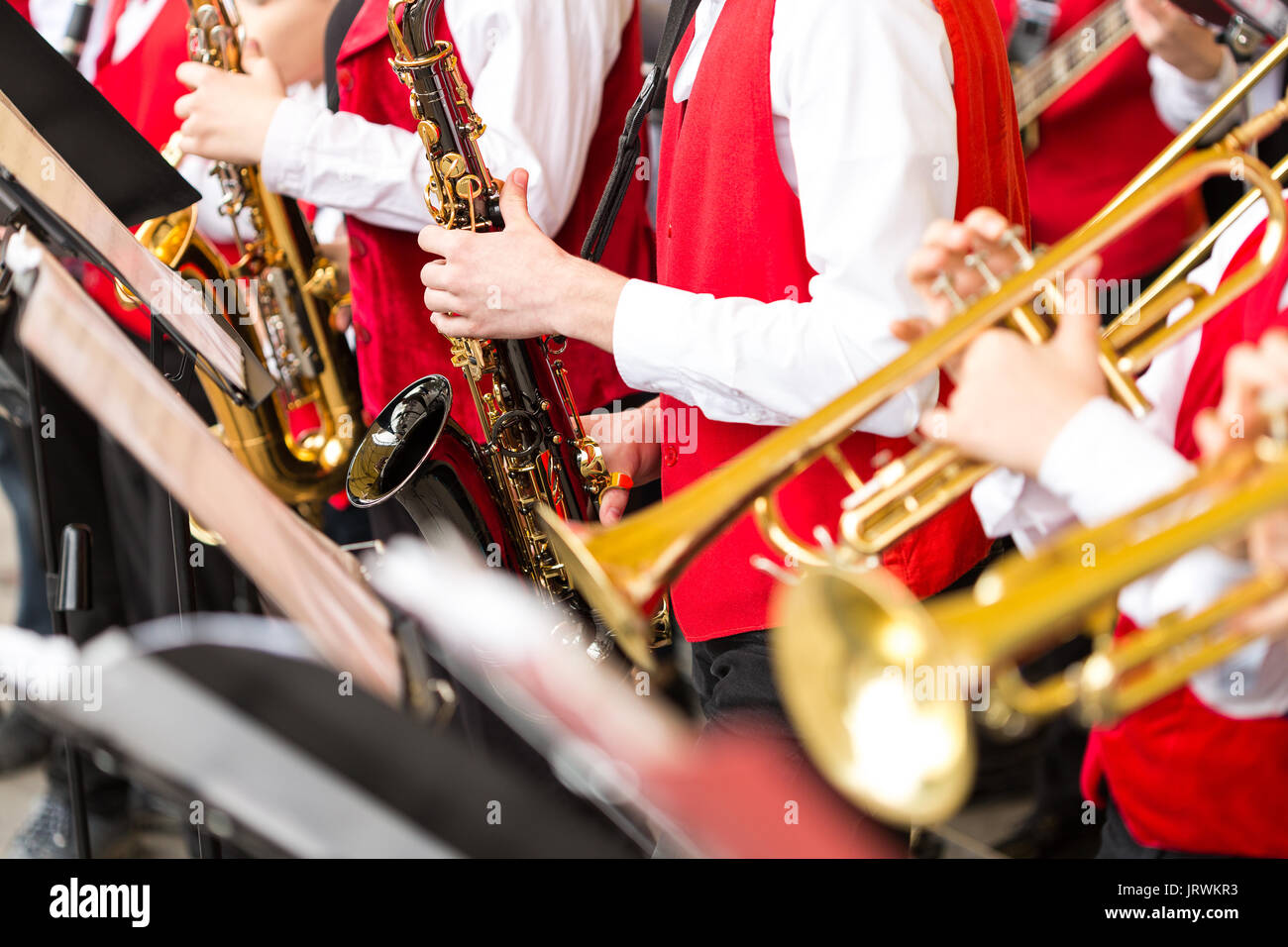jazz band music performance concept - orchestra of wind instruments during  the concert, selective focus on hands of musicians playing on trumpets and  saxophones, closeup male in red costumes Stock Photo - Alamy