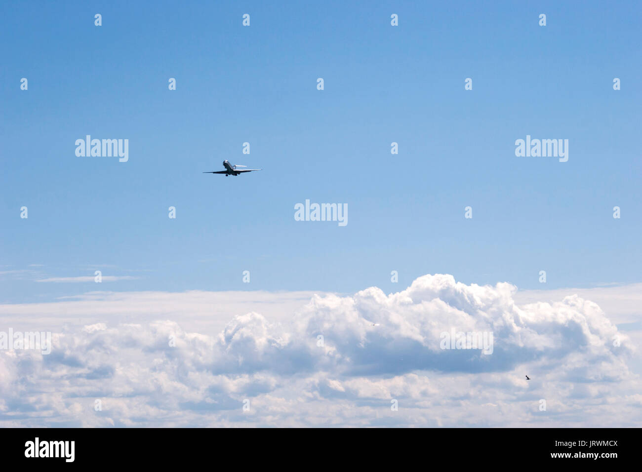 Airplane flying across a blue sky above white clouds Stock Photo - Alamy