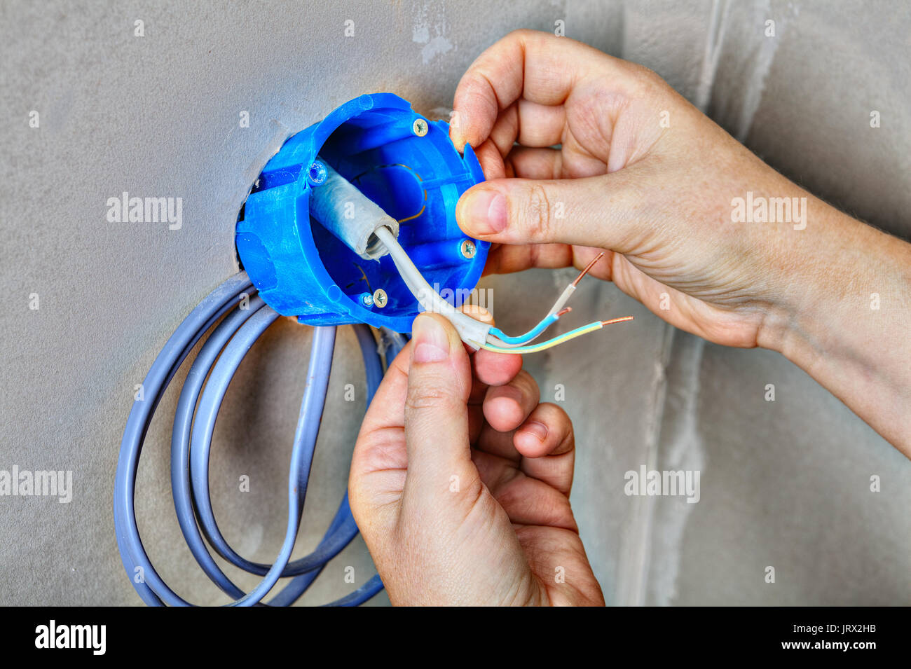 Hands electrician fix electricity round plastic outlet box on wall