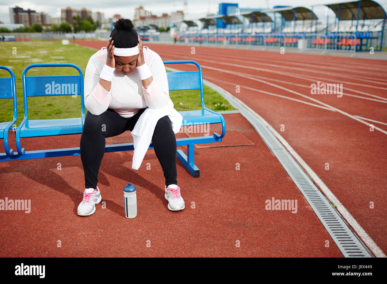 Chubby woman recovering after tough workout at track and field stadium Stock Photo