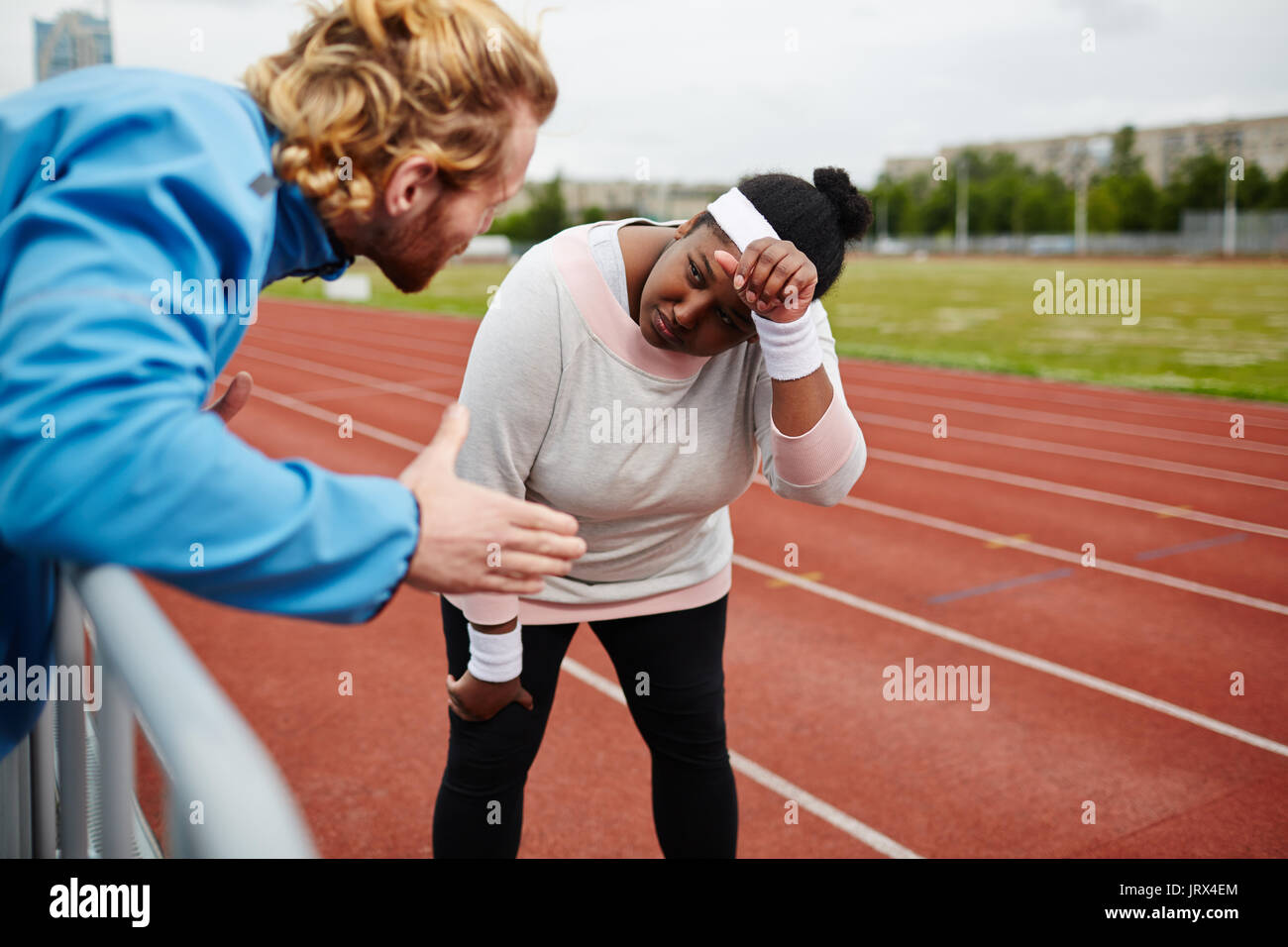 Tired plus-size woman being motivated by personal trainer on running track Stock Photo