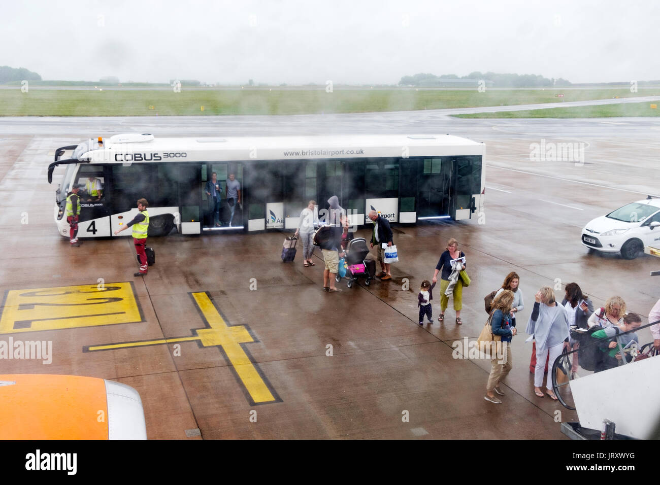 Passengers leaving a transit bus to board an Easy Jet plane in the rain on a dull wet morning at a UK airport Stock Photo