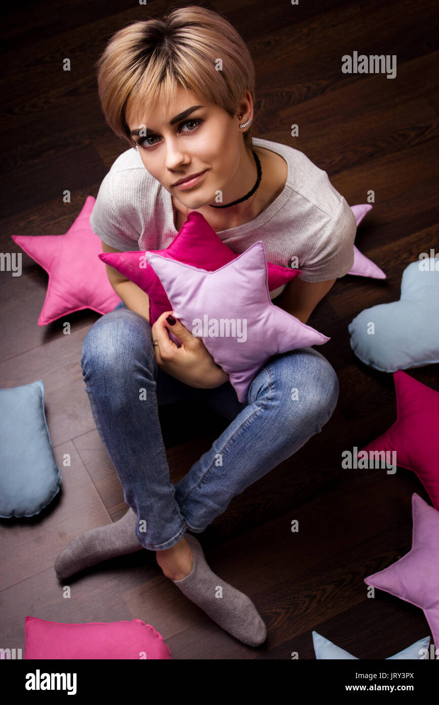 Attractive young woman looking in camera on the dark parquet with pillows Stock Photo