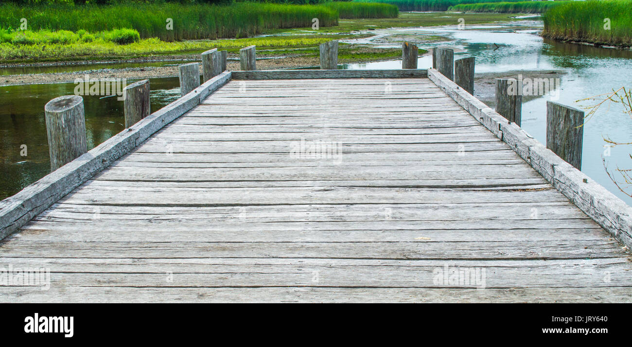 weathered gray wooden dock extending into river surrounded by greenery Stock Photo