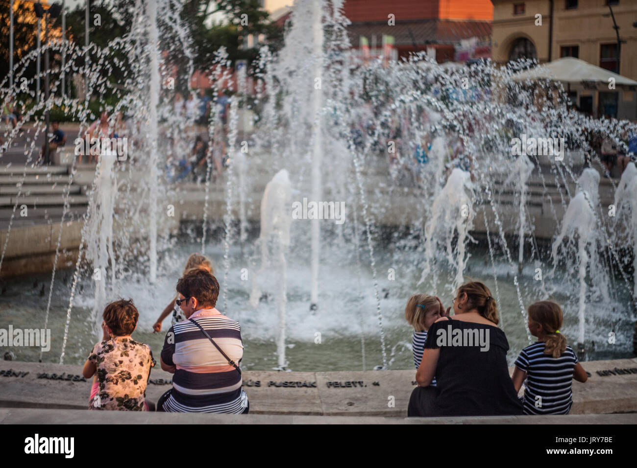 SZEGED, HUNGARY - JULY 22, 2017: Foutain on Dugonics Ter Square with children playing in front with their grandmothers. This square, and the universit Stock Photo